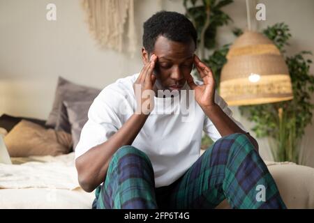 Young african man having headache sitting on bed Stock Photo