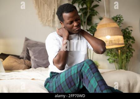 African stressed, unhappy man with really bad neck pain, after waking up at the morning. Stock Photo