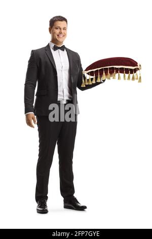 Full length portrait of young man in a suit and bow tie holding a red velvet cushion isolated on white background Stock Photo