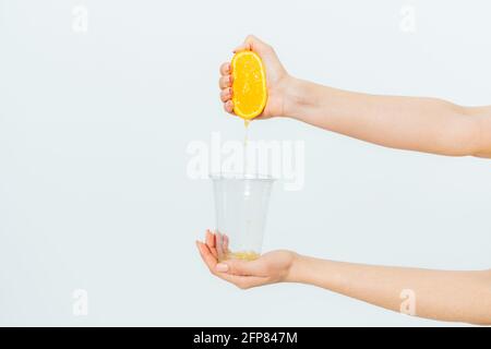 Woman's hand squeezing orange juice from fresh orange into transparent glass on white background. Stock Photo