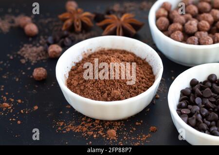 Cocoa powder and chocolate morsels in bowls on dark slate table, dessert cooking ingredients background Stock Photo