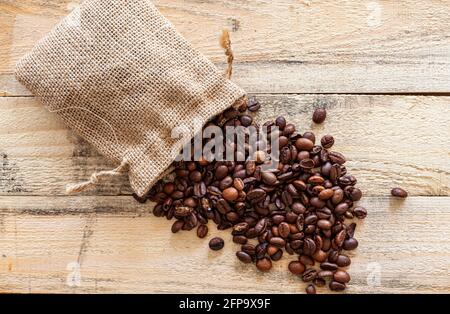 Small overturned sack from which coffee beans come out on a wooden plank surface. Stock Photo