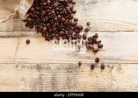 Small sack overturned on some pine wood boards where many roasted coffee beans are roasted. Stock Photo