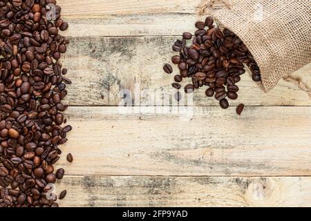 Small overturned sack from which coffee beans come out on a wooden plank surface with a margin of coffee beans on the left. Stock Photo