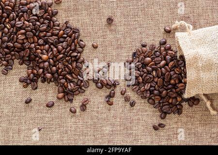 Small overturned sack with coffee beans on a sackcloth surface on which there are already more grains. Stock Photo