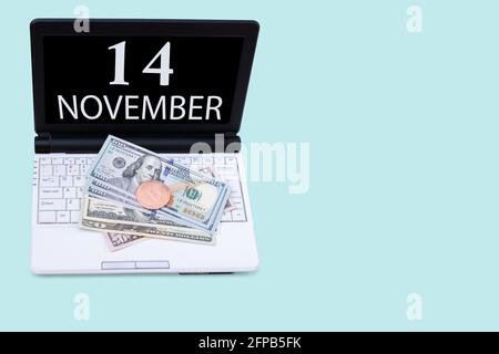 14th day of november. Laptop with the date of 14 november and cryptocurrency Bitcoin, dollars on a blue background. Buy or sell cryptocurrency. Stock Stock Photo