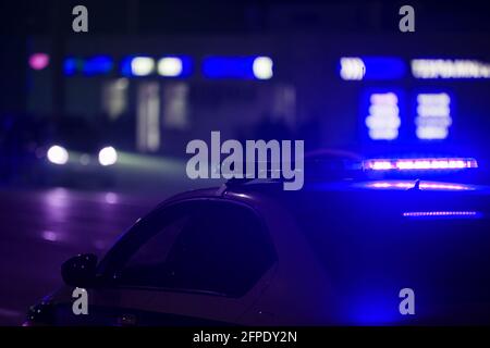 blue police car light at night in city with selective focus and blurry car in the background. Stock Photo