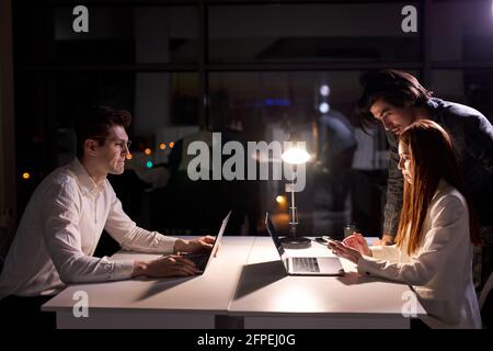 Creative caucasian people working at night in boardroom, coworkers working on computer at table in startup office, miss the deadline. brainstorming, b Stock Photo