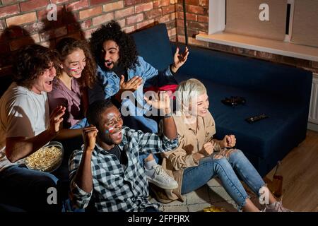 Young People Watching Sport Celebrating Goal, While Watching Competition On TV Online Translation. Cheering For Favourite Team, Entertainment Concept Stock Photo