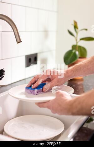 cropped man washing dishes at home kitchen. close-up male hands doing household. unrecognizable man holding sponge and washing plates Stock Photo