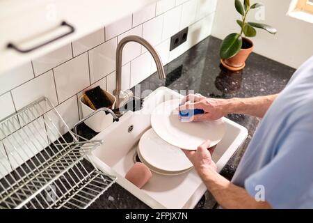 cropped man washing dishes at home kitchen. close-up male hands doing household. top view on man holding sponge and washing plates Stock Photo