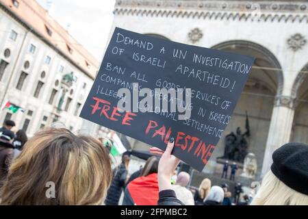 Aktivistin hält Schild mit der Aufschrift: ' Forderung nach einer UN Untersuchung der Apartheid in Israel! Verbot aller Waren und Dienstleistungen aus Israels illegalen Kolonialsiedlungen/Free Palestine '. Ca. 600 Menschen versammelten sich am 20.5.2021 in München, um ihre Solidarität mit den Menschen in Gaza, Ost Jerusalem, den besetzten Gebieten und dem Westjordanland zu zeigen. - Activists holds sign reading: ' Demand a UN Investigation of Israeli Apartheid! Ban all goods/services of companies operating in Israel'S illegal colonial sttlements/Free Palestine '. Around 600 people gather Stock Photo