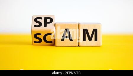 Spam and scam symbol. Turned a wooden cube and changed the word 'scam' to 'spam' or vice versa. Beautiful yellow table, white background, copy space. Stock Photo