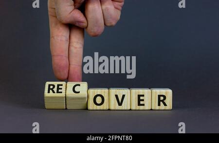 Time to recover symbol. Businessman turns wooden cubes and changes the word 'over' to 'recover'. Beautiful grey table, grey background. Business, over Stock Photo