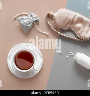 Quality of sleep. Sleep mask, sleeping pills, scented candle and cup of calming tea. Two tone silver gold beige paper flat lay. Top view, square Stock Photo