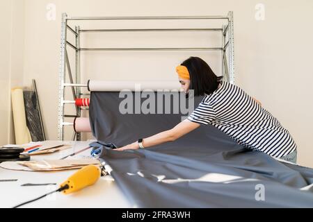 Young tailor take roll of fabric to cur pattern textile measure working on new collection in atelier Stock Photo
