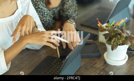 Side view of businesswomen hands pointing on tablet screen while consulting on their project Stock Photo