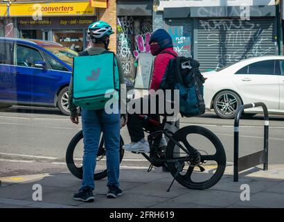 London. UK- 05.18.2021: two young man working as self employed home delivery riders working for online food ordering companies having a chat. Stock Photo