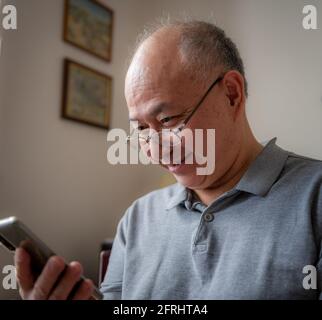 A smiling, laughing elderly Asian man enjoying using social media at home. Stock Photo
