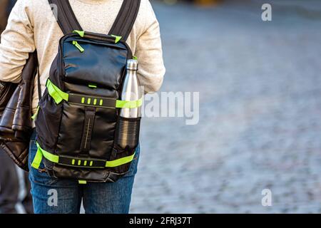 a man with a backpack with a bottle of water from behind on a defocused street background, close-up Stock Photo