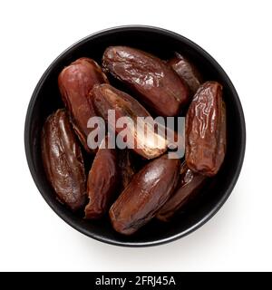 Dry pitted dates and one half date in a black bowl isolated on white. Top view. Stock Photo