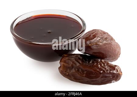 Date syrup in a glass bowl next to two whole dry pitted dates isolated on white. Stock Photo