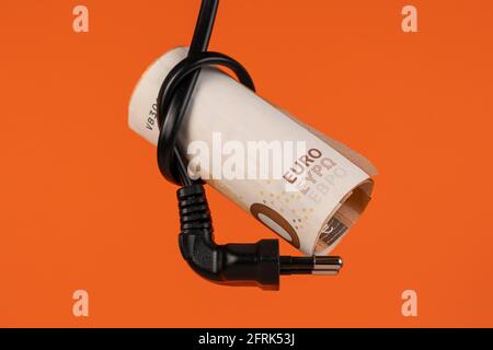 Euro money in an electrical cord knot with a plug close up. Home finance concept. Cash banknotes. On a colored creative terracotta orange background. Stock Photo