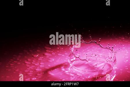 Beautiful splash crown from a drop of water falling on a hard surface. In red light on a black background Stock Photo