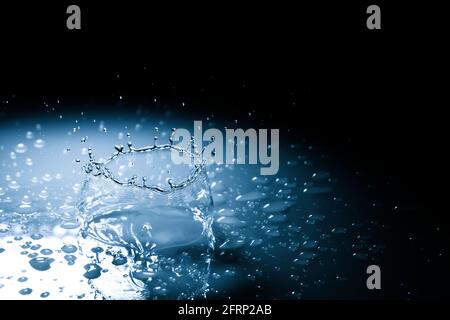 Beautiful splash crown from a drop of water falling on a hard surface. In blue light on a black background Stock Photo