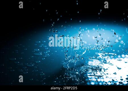 Beautiful splash blue background a drop of water crashed on a hard surface. In blue light on a black Stock Photo