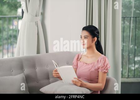 Beautiful young woman reading magazine and lying on sofa at home Stock Photo