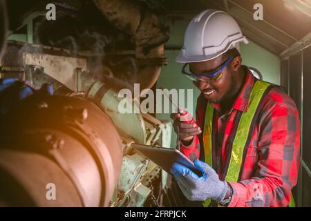 African engineering engine machine controller checking, working with tablet and talking on radio communication to tell worker working in industry Stock Photo
