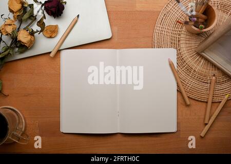 Top view of workspace with opened blank notebook, stationery and flower decorated on wooden table Stock Photo