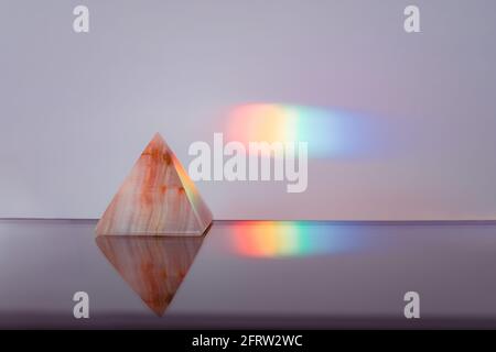 Agate pyramid with a rainbow streak background on a reflective surface Stock Photo