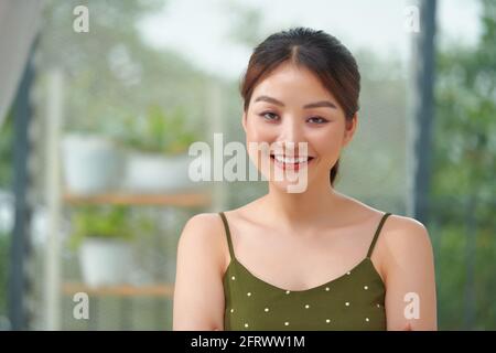 Relaxed smiling friendly woman sitting perched on the edge of a table in her living room Stock Photo