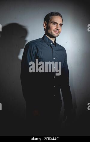 An influencer, artist and musician, dress with black shirt, poses for the camera in one of his photographic shootings for social networks, in a dark b Stock Photo