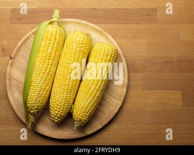 Top view of corns and corn on the cop on wooden plate on wooden table with copy space Stock Photo