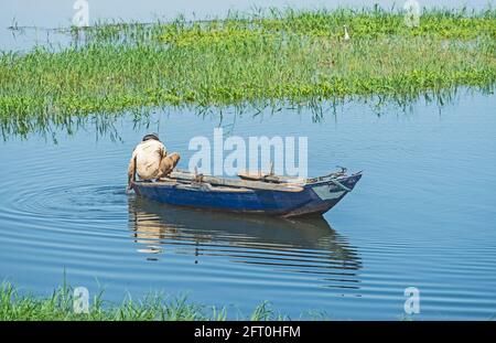 Traditional egyptian bedouin fisherman in rowing boat on river Nile fishing by riverbank Stock Photo