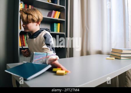 Close-up low-angle view of angry child boy dropping things off the desk in cozy light children room during doing homework Stock Photo