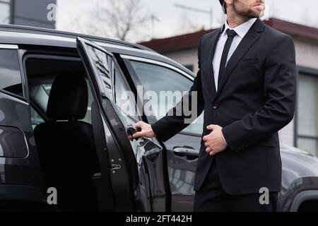 partial view of bearded bodyguard with security earpiece opening car door