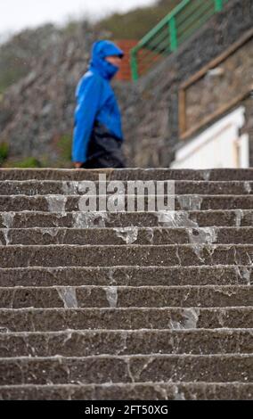 Swansea, UK. 21st May, 2021. A man walks past the steps onto the beach as rainwater cascades down them at Langland Bay near Swansea this afternoon during the wet and windy weather. Credit: Phil Rees/Ģ����ý Live News Stock Photo