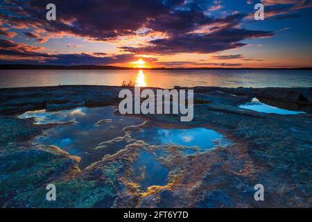 Striking and colorful sunset with golden hour light on colorful rock and small pools at the lakeside of Vansjø In Østfold, Norway, Scandinavia. Stock Photo