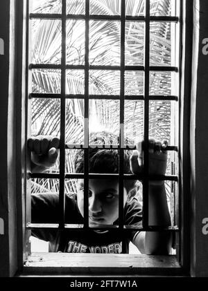 a close shot of Indian boy looking in window house monochrome vertical frame, Kalaburagi, Karnataka, India-May 10.2021 Stock Photo