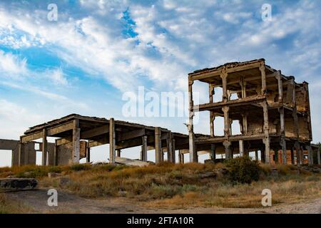 Old abandoned unfinished emergency building damaged by time, wind and rain against the background of a blue sky with white clouds. Ruins of building. Stock Photo
