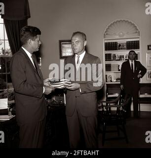 President John F. Kennedy receives a gift of an American flag from astronaut Lieutenant Colonel John H. Glenn, Jr. (right); Lt. Col. Glenn carried the flag in his space suit during his orbital flight aboard Mercury-Atlas 6, also known as Friendship 7. Special Assistant to the President, Kenneth P. O'Donnell, stands in the background. Oval Office, White House, Washington, D.C. Stock Photo