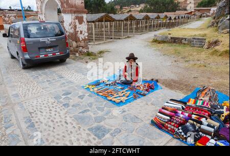 An old woman in local dress sits roadside selling tourist souvenirs, Chinchero, an Andean village in the Sacred Valley, Urubamba, Cusco Region, Peru Stock Photo