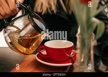 Woman's hand pours tea from glass teapot into cup in street cafe Stock Photo