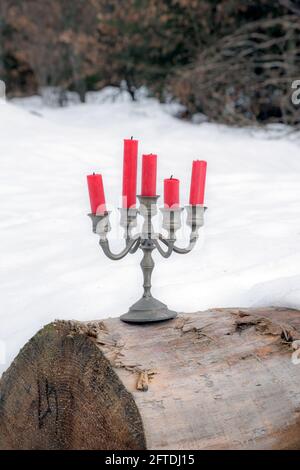 pewter candelabra with five red candles stands on a tree trunk outside in winter Stock Photo