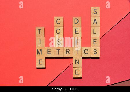 Metrics, time, cost, define, sales, words in wooden alphabet letters in crossword form isolated on red Stock Photo