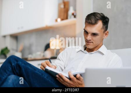 young man taking notes sitting on the couch . Stock Photo